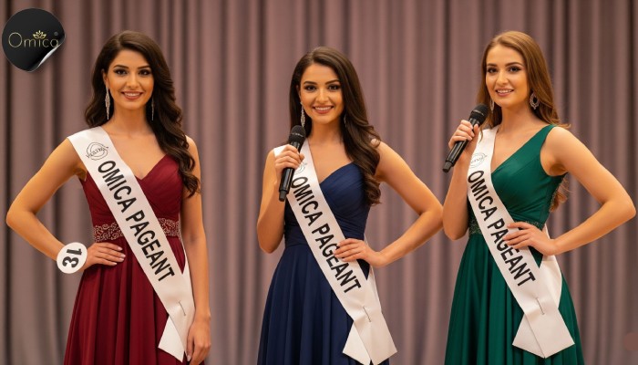 Three Indian beauty pageant contestants wearing OMICA PAGEANT sashes on stage with a soft Omica Pageant logo in the background.