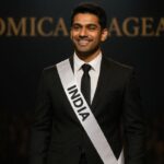 AI-generated image of a confident Indian male contestant at Omica Pageant, standing on stage in a black suit under spotlight with blurred audience in the background.